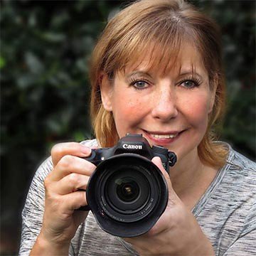 Jan smiling while holding a Canon DSLR camera positioned forward as if taking a photo.
