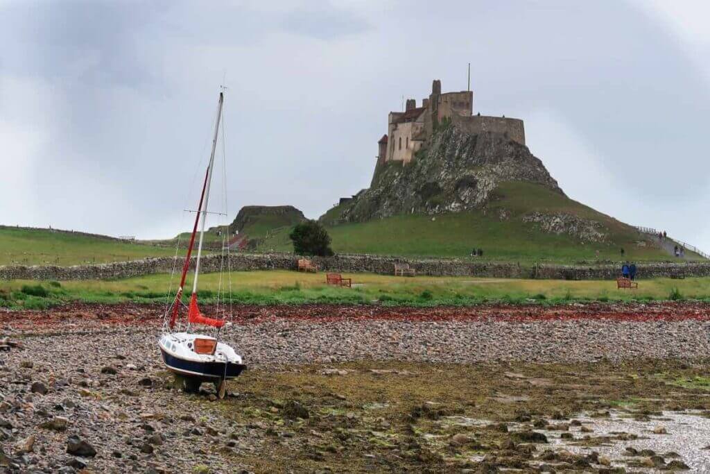 Beached yacht on the Holy Island shoreline with Lindisfarne Castle in the background