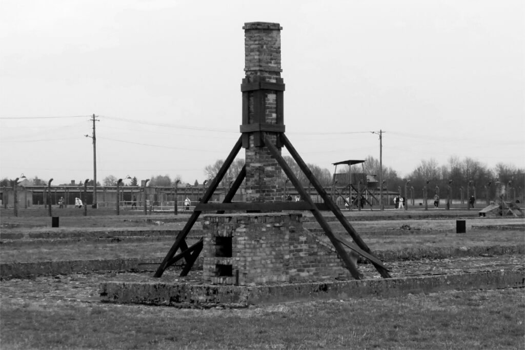Black and white photograph of a lone brick chimney with wooden braces at Auschwitz-Birkenau.